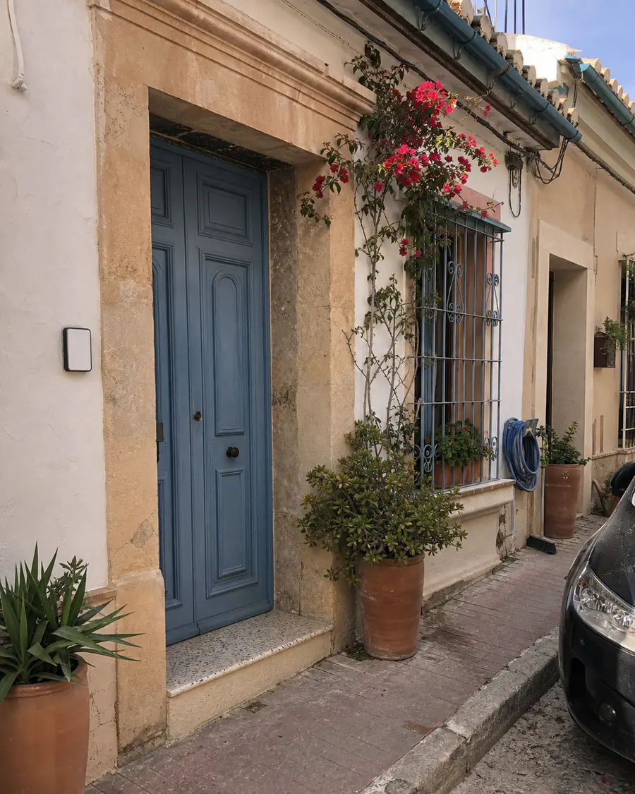 A sunlit Spanish townhouse with a blue front door and bougainvillea