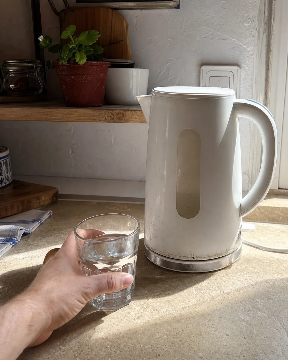 A glass of tap water beside a kettle with limescale in a Mallorcan kitchen